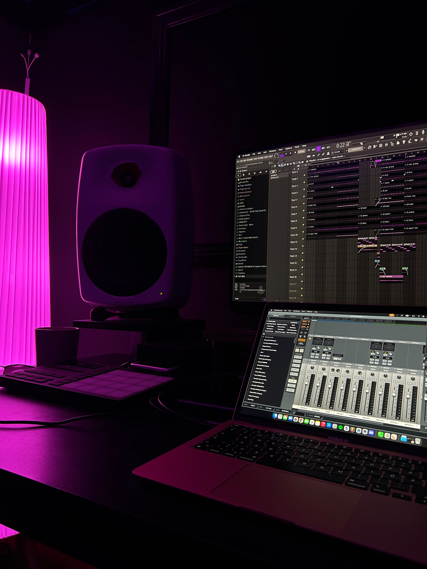 A studio desk at night with a glowing pink lamp, a speaker and a laptop with a mixing console open